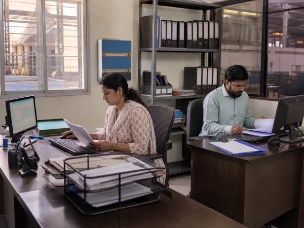 Administrative staff at their desks with document files on the shelving behind