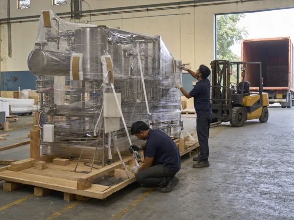 Workers securing a wrapped machine to a wooden export skid at the dispatch bay